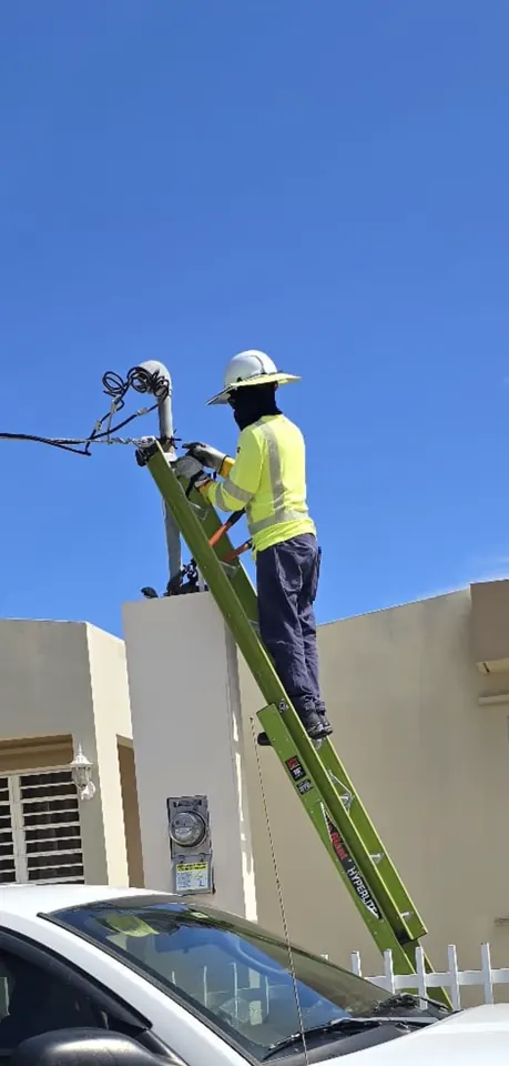 Electrician on a ladder working on the service entrance and meter of a home